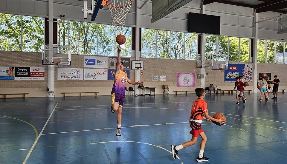 Jóvenes jugando a baloncesto en el polideportivo cubierto durante el campamento de verano en inglés